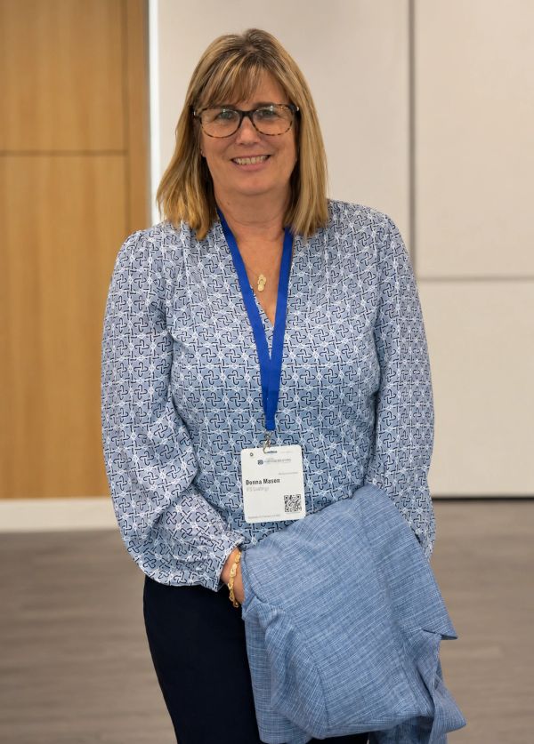 Smiling woman with glasses and name badge holding a jacket.