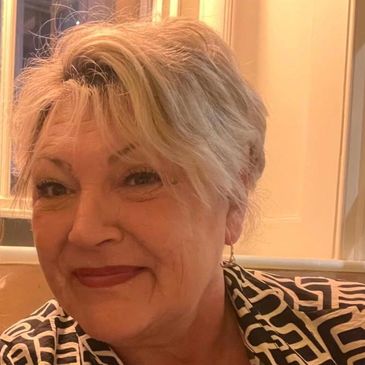 Smiling woman with short blonde hair and patterned blouse indoors.