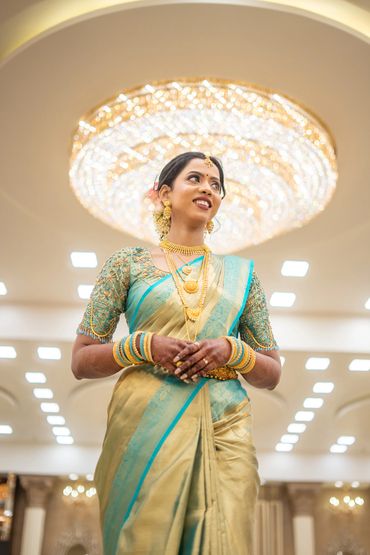 A smiling woman in traditional attire stands under a grand chandelier.