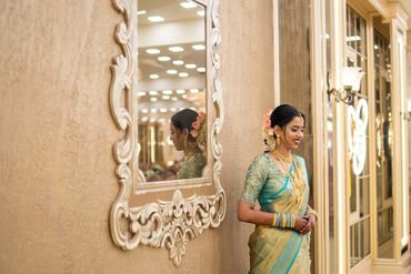 A woman in traditional attire stands smiling near an ornate mirror.