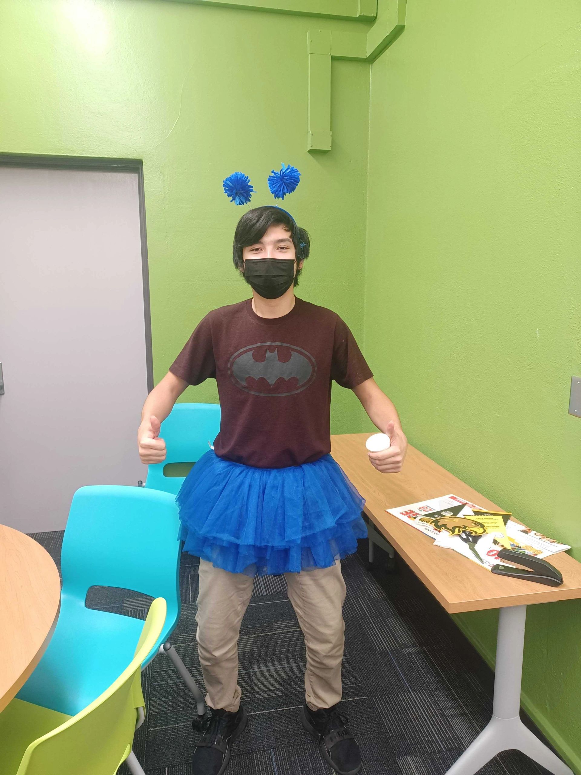 Person in blue tutu and headband giving thumbs up.