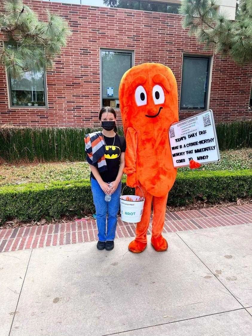 Person posing with a carrot mascot holding a whiteboard.