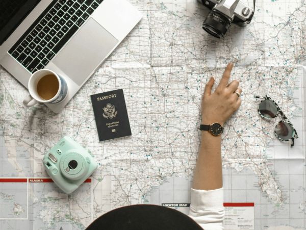 A woman at a table with maps before her and her laptop, planning a trip.