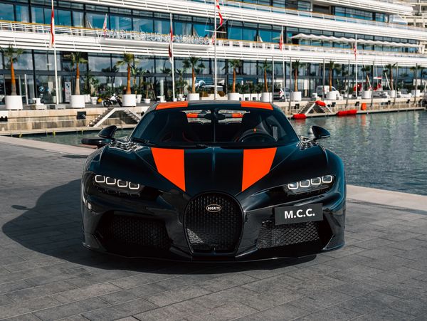 Black Bugatti with orange stripes parked by the waterfront.