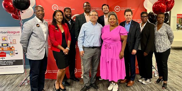 Group of diverse professionals posing at an Urban League event with red backdrop and balloons.
