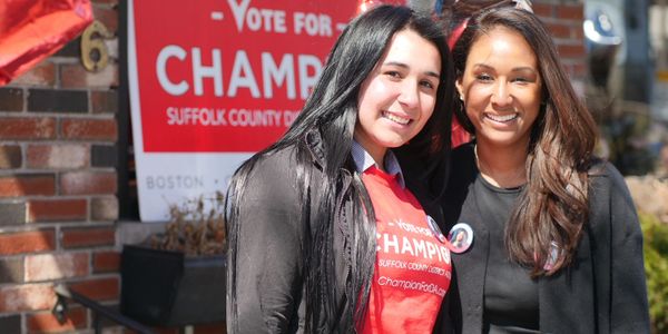 Two women smiling in front of a campaign sign.