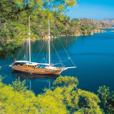 A wooden sailboat anchored in calm blue waters surrounded by greenery.