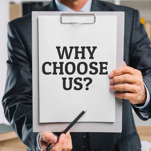 Businessman holding clipboard with 'Why Choose Us?' sign and pointing pen.