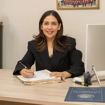 Woman in black blazer working at a desk with documents and computer.