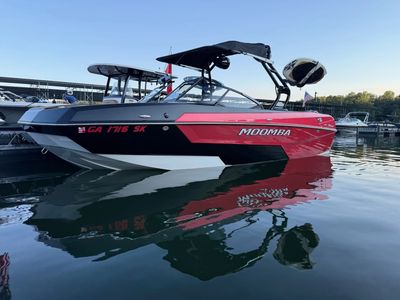 Red and black Moomba boat docked with water reflections under clear sky.