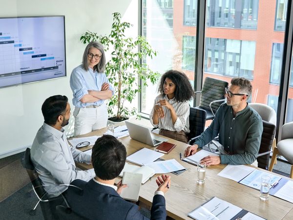 A diverse group of professionals engages in a meeting around a conference table, with a presentation
