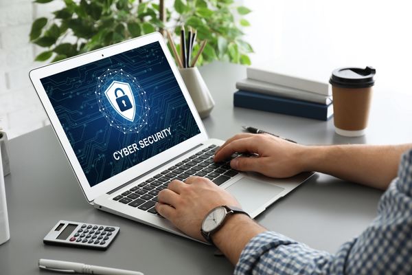 A person typing on a laptop displaying a cyber security graphic, with a calculator and coffee cup