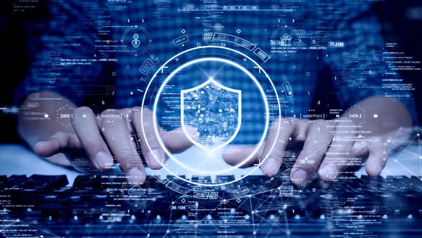 A close-up of hands typing on a keyboard surrounded by a digital shield, symbolizing cybersecurity