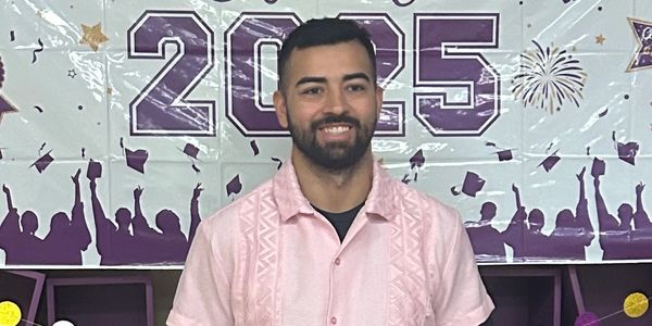 Man smiling in front of a 2025 graduation banner.