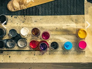 Various paint colors in small containers arranged on tape.