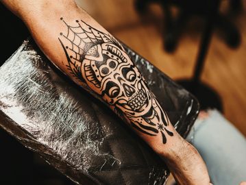 Black ink skull tattoo with spider web on forearm.