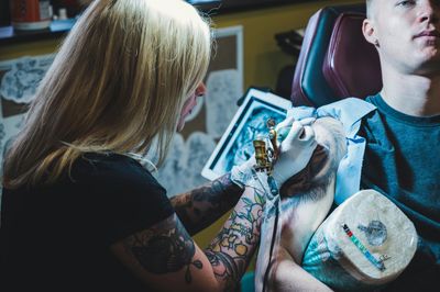 Tattoo artist working on a detailed tattoo on a man's arm.