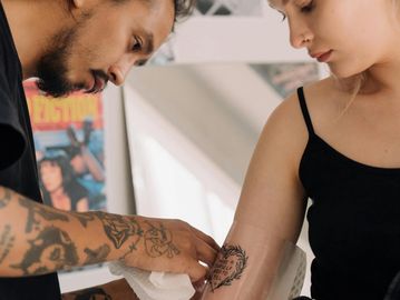 Tattoo artist carefully applying a new tattoo to a woman's arm.