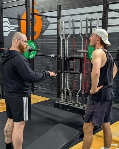 Two men talking in a gym with weightlifting equipment around.