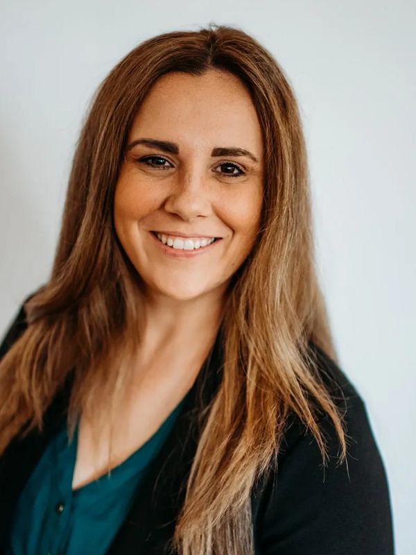 Smiling woman with long hair wearing a teal top and black blazer.