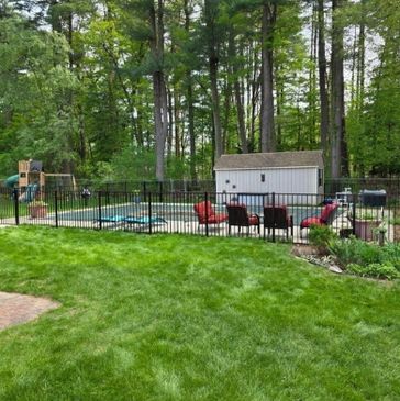 Backyard with a fenced pool, patio chairs, and a shed surrounded by trees.