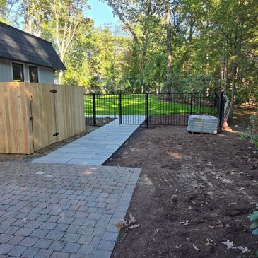 Newly paved pathway and fenced backyard with fresh wooden gate and green lawn.