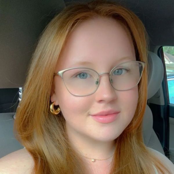 Woman with red hair and glasses smiling in a car.