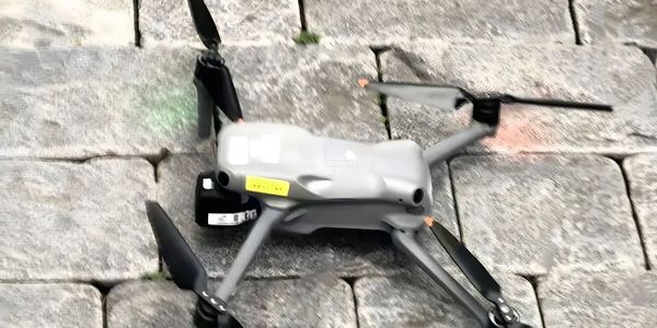 A gray drone with four propellers resting on stone pavement.