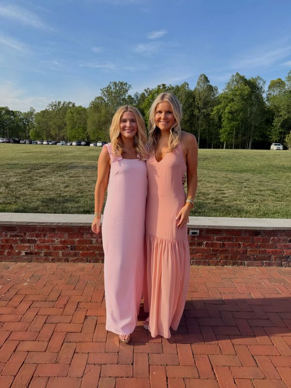 Two women in elegant pink dresses standing outdoors on a brick pavement.