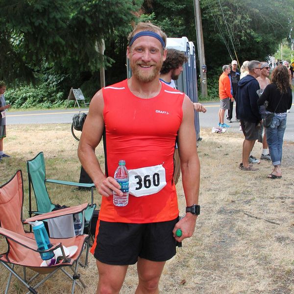 Smiling man in red athletic shirt at outdoor event.