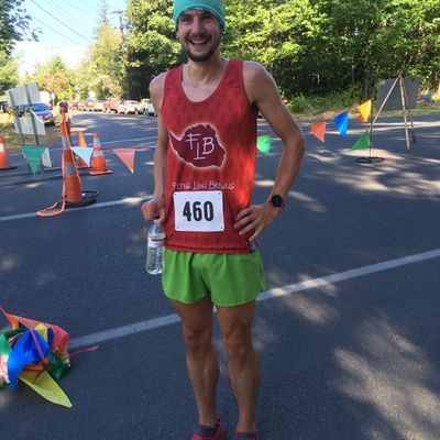 Smiling runner in green shorts, red tank, and blue cap holding water at race event.
