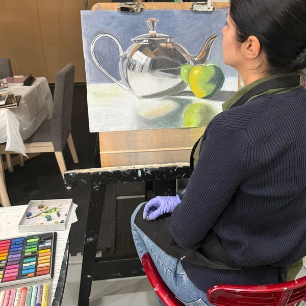 Artist painting a realistic still life of a teapot and apple.