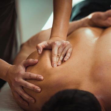 Hands giving a deep shoulder massage to a person lying face down.