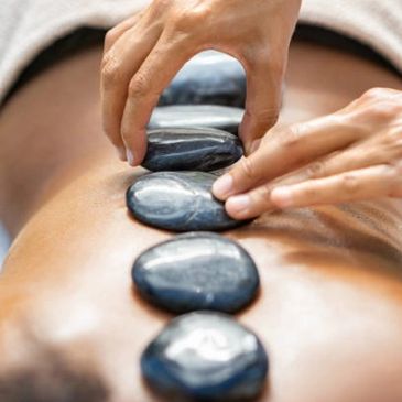 Hands placing hot stones on a person's back for massage therapy.