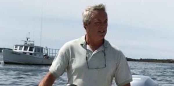 Man steering a small boat on calm water with another boat in background.