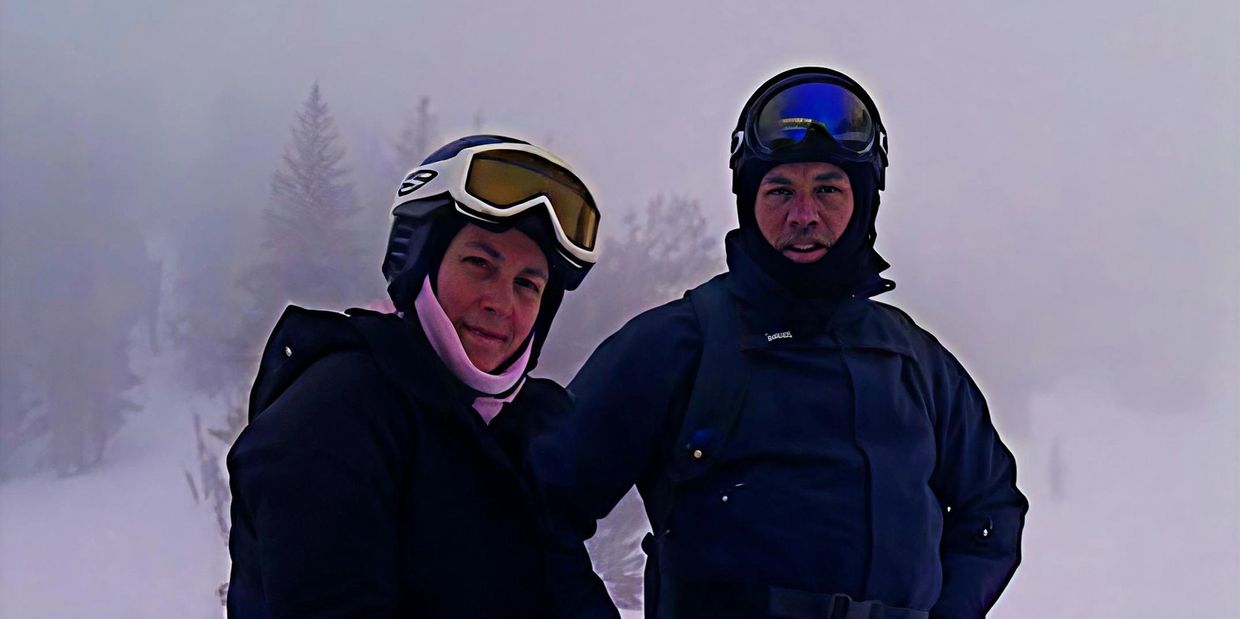 Two people in ski gear standing in a snowy, foggy environment.
