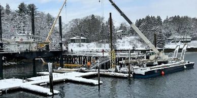 Snow-covered dock and cranes by a calm waterfront in winter.
