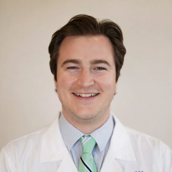 Smiling man in a white coat and green striped tie.