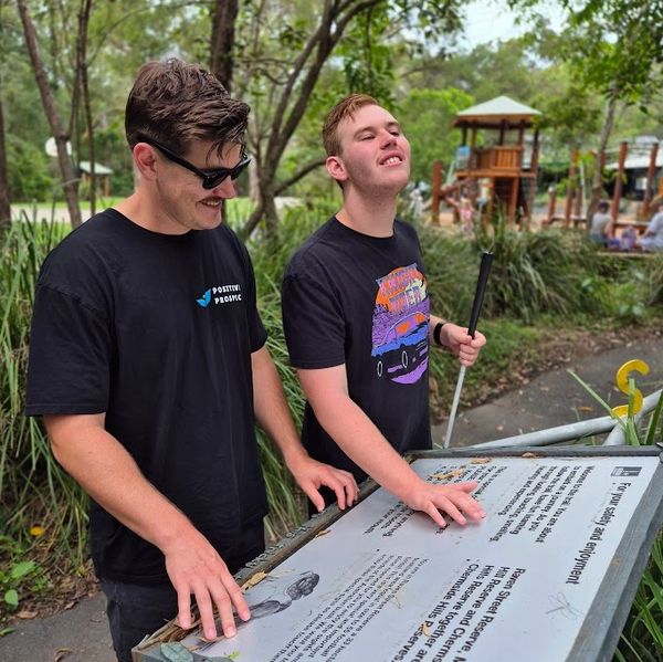 Lucas supporting Wil to read braille on accessible signage at Downfall Creek Environmental Centre.