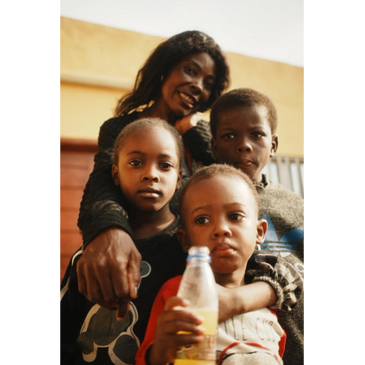A smiling woman with three children, one holding a bottle.