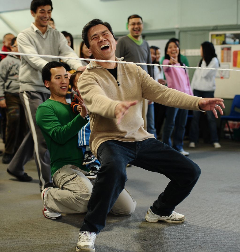 Group of people laughing and playing tug-of-war indoors.