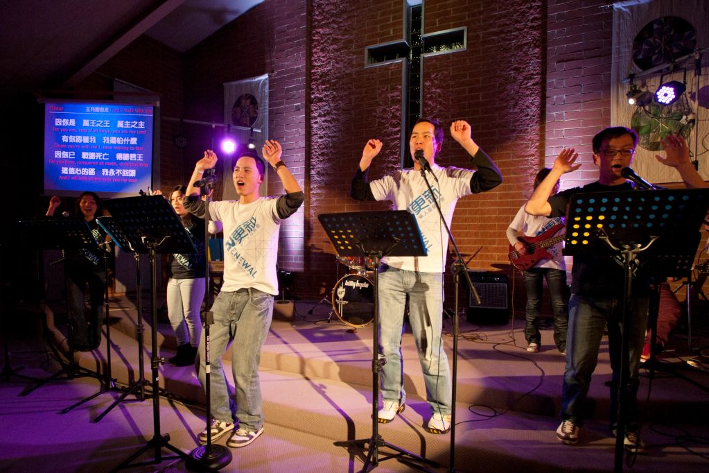 A church worship band passionately singing on stage with a cross backdrop.