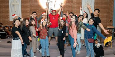 Group of young people posing joyfully indoors, some wearing Santa hats.