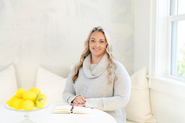 Woman in cozy sweater sitting at a white table with lemons and a notebook.