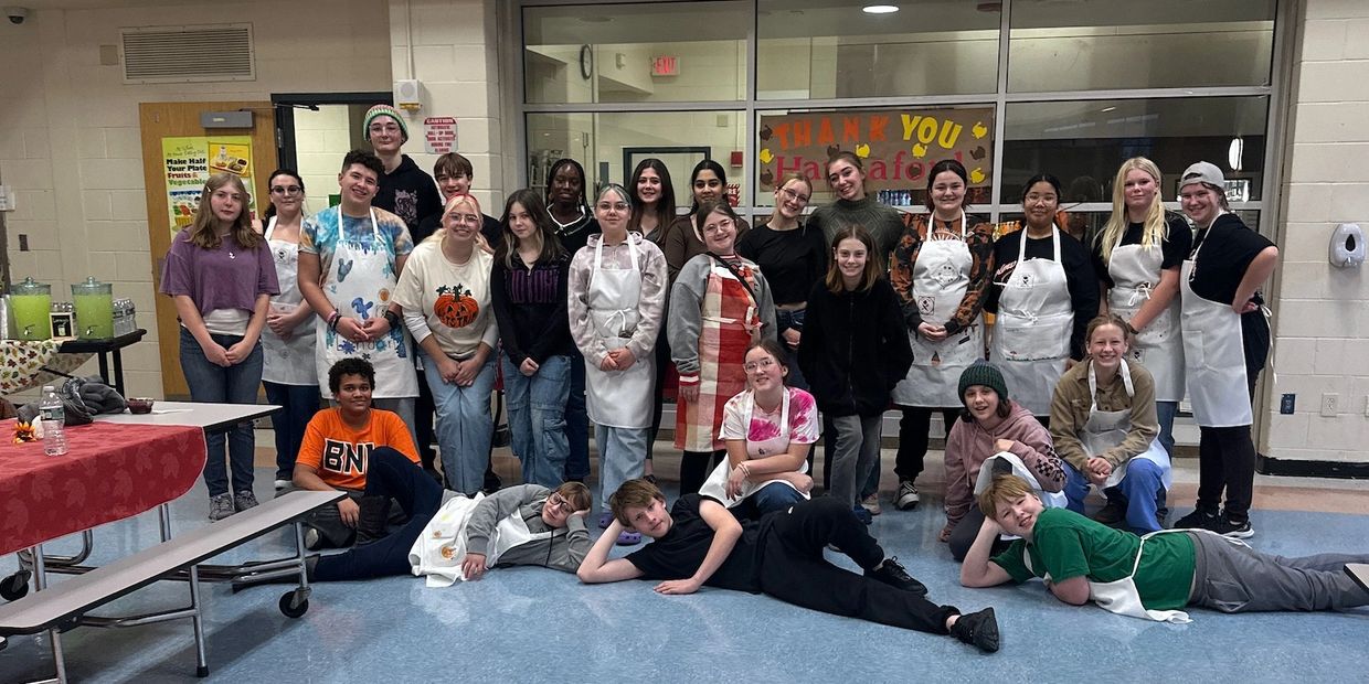 Group photo of young people in aprons in a cafeteria setting.