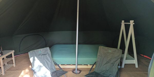 Cozy tent interior with a bed, two camp chairs, and a small table.