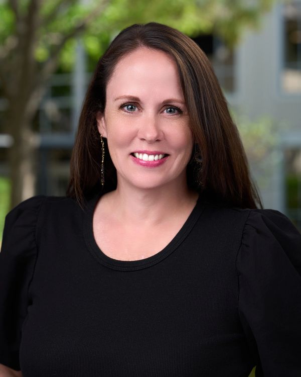 Woman with long brown hair smiling in a black shirt.