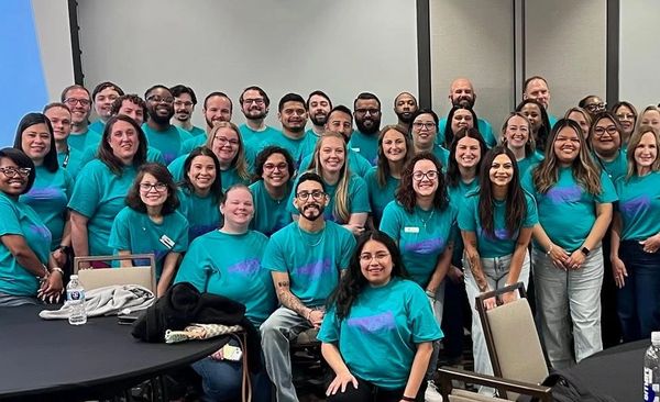 Large group of people smiling in matching teal shirts.