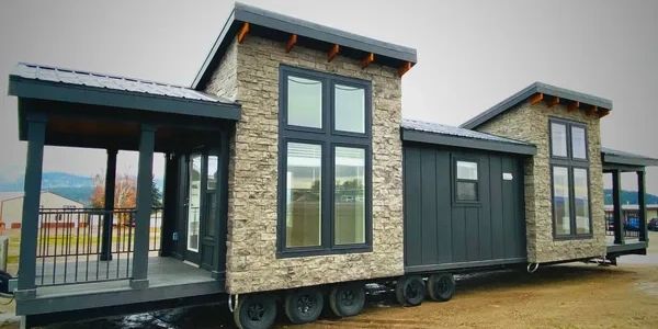Modern tiny house on wheels with stone and dark panel exterior.