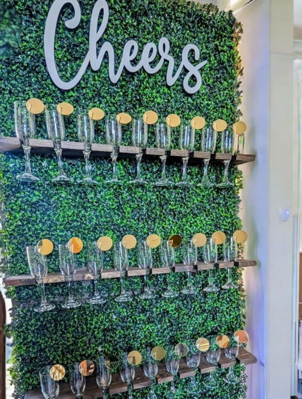 Wall display with champagne glasses and a "Cheers" sign on greenery background.